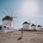 Iconic windmills of Mykonos with tourist walking, blue sky in the background - best time to visit