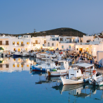 Traditional fishing boats at Naoussa harbor in Paros, one of the most charming Greek villages to visit in 2026, featuring whitewashed architecture at sunset.